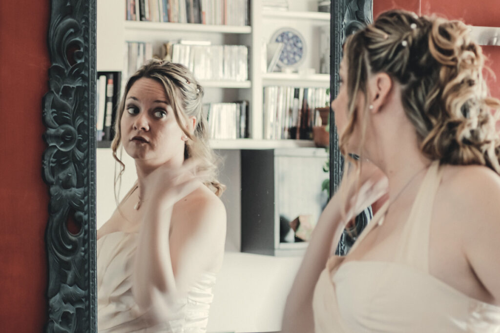 Blonde bride with wedding dress looks at the mirror during the preparation