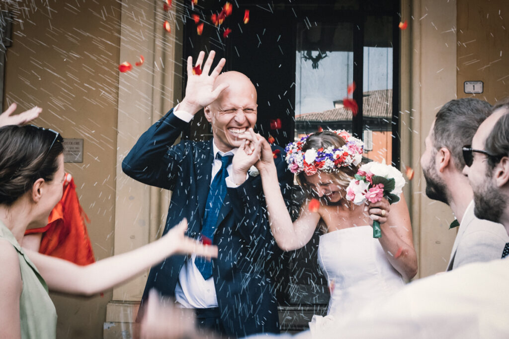 just married, happy couple is inundated with rice and red petals 