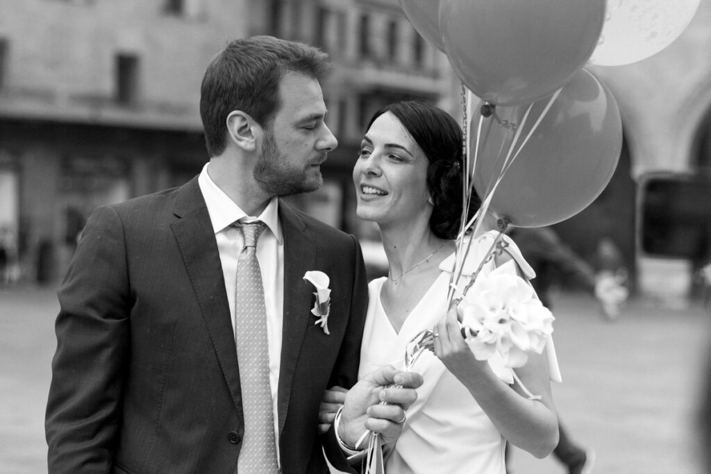 the spouses walk in piazza Maggiore in Bologna smiling and with balloons