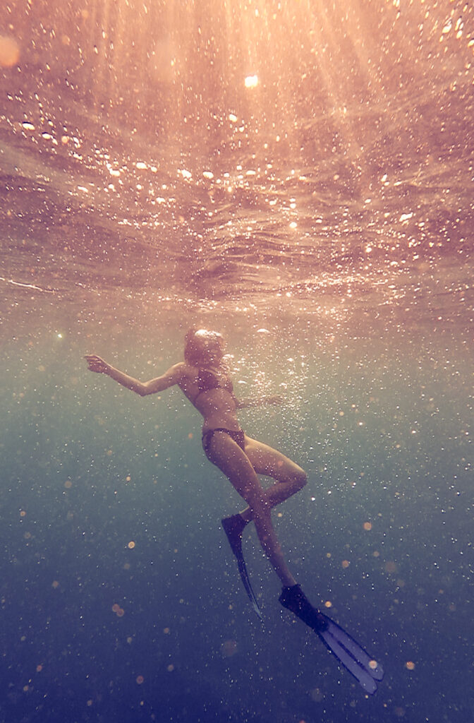 woman diving on the ocean water colored by the sun rays, underwater