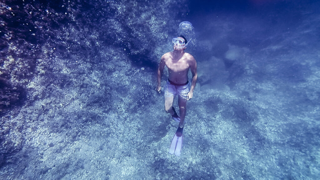 A man diving on the blue ocean with the backdrops in the background, bubbles in the water