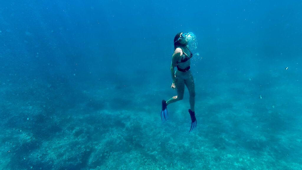 A woman diving in the blue and deep water, bubbles in the water